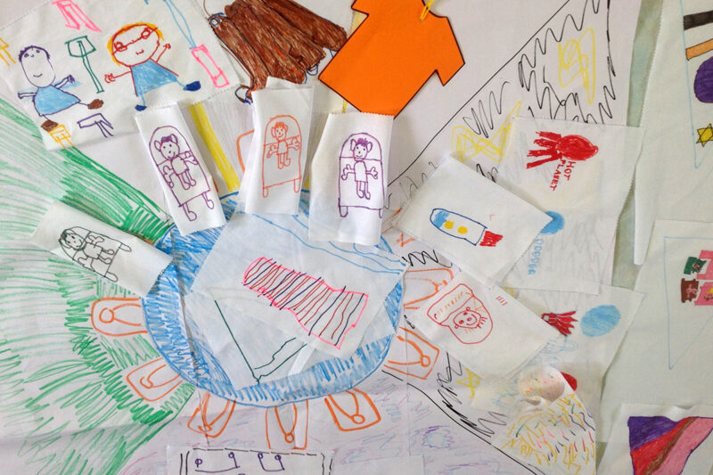 photo:lots of colourful drawings on pieces of white cloth are jumbled up together. We can make out some stick people and an octopus - all on different bits of cloth.