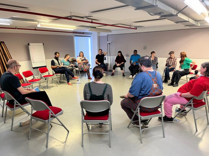 a group image of lots of people sat in a big circle on chairs